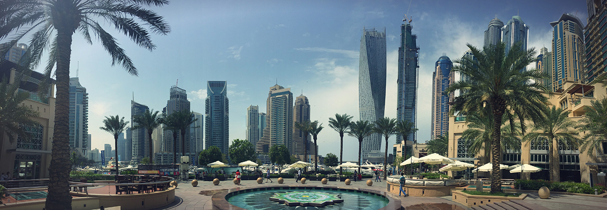 Foto von einem Platz in Dubai mit zahlreichen Wolkenkratzern rundherum. Dazwischen Palmen, kleine Brunnen und Plätze mit Sonnenschirmen zum Ausruhen